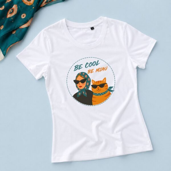 Bela ženska majica Be Cool, Be Mjau sa ilustracijom žene i narandžaste mačke sa sunčanim naočarima na pastelno plavoj pozadini.