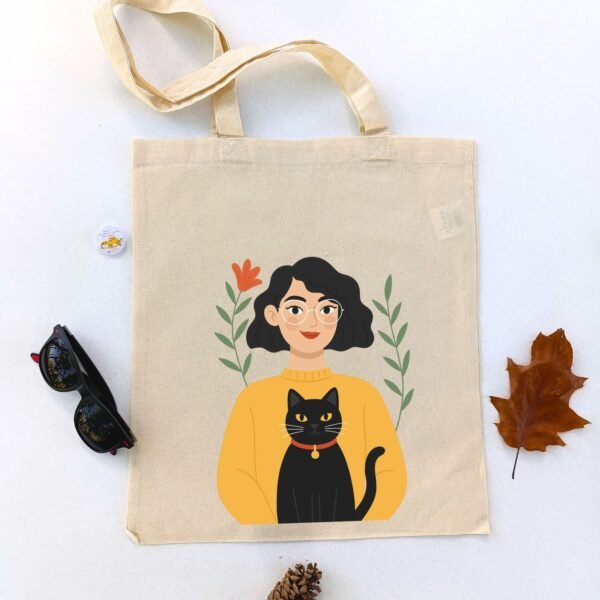 Ceger Mačkasta Ja sa ilustracijom žene sa kratkom crnom kosom i naočarima, u žutom džemperu sa crnom mačkom u naručju. Poklon za ljubitelje mačaka.