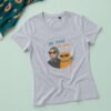 Siva ženska majica Be Cool, Be Mjau sa ilustracijom žene i narandžaste mačke sa sunčanim naočarima na pastelno zelenoj pozadini.