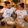Par nosi Cat Dad i Cat Mom majice dok sedi na kauču sa mačkom između njih