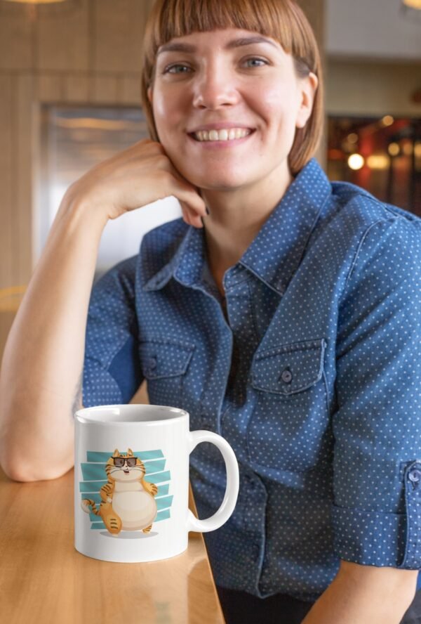 Žena u plavoj košulji sa osmehom drži Mačketina šolju sa natpisom „Pas ima gospodara, mačka ima osoblje“.