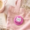 Roze Mačkoljubica bedž sa ilustracijom mačke na roze cegeru uz kafu i knjigu – cozy dodatak za ljubitelje mačaka