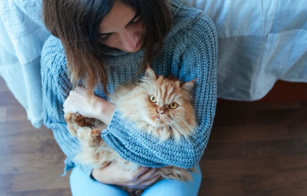 Žena drži mačku u naručju dok je mačka mirna i gleda ispred sebe, pokazujući osećaj sigurnosti i poverenja – Mačka Vas Posmatra Dok Spavate – Evo Šta To Zaista Znači