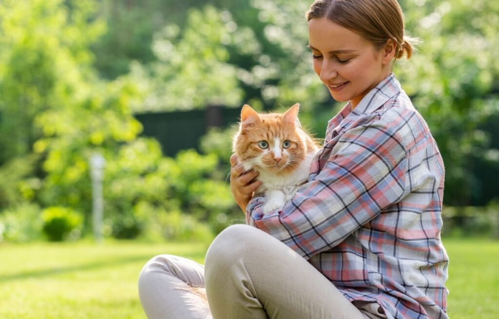 Kako mačke biraju svog čoveka – žena drži narandžastu mačku u naručju dok uživaju u mirnom trenutku poverenja i bliskosti na otvorenom